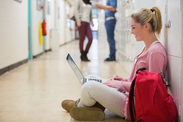 Woman sitting on the floor at the hallway holding a laptop and smiling